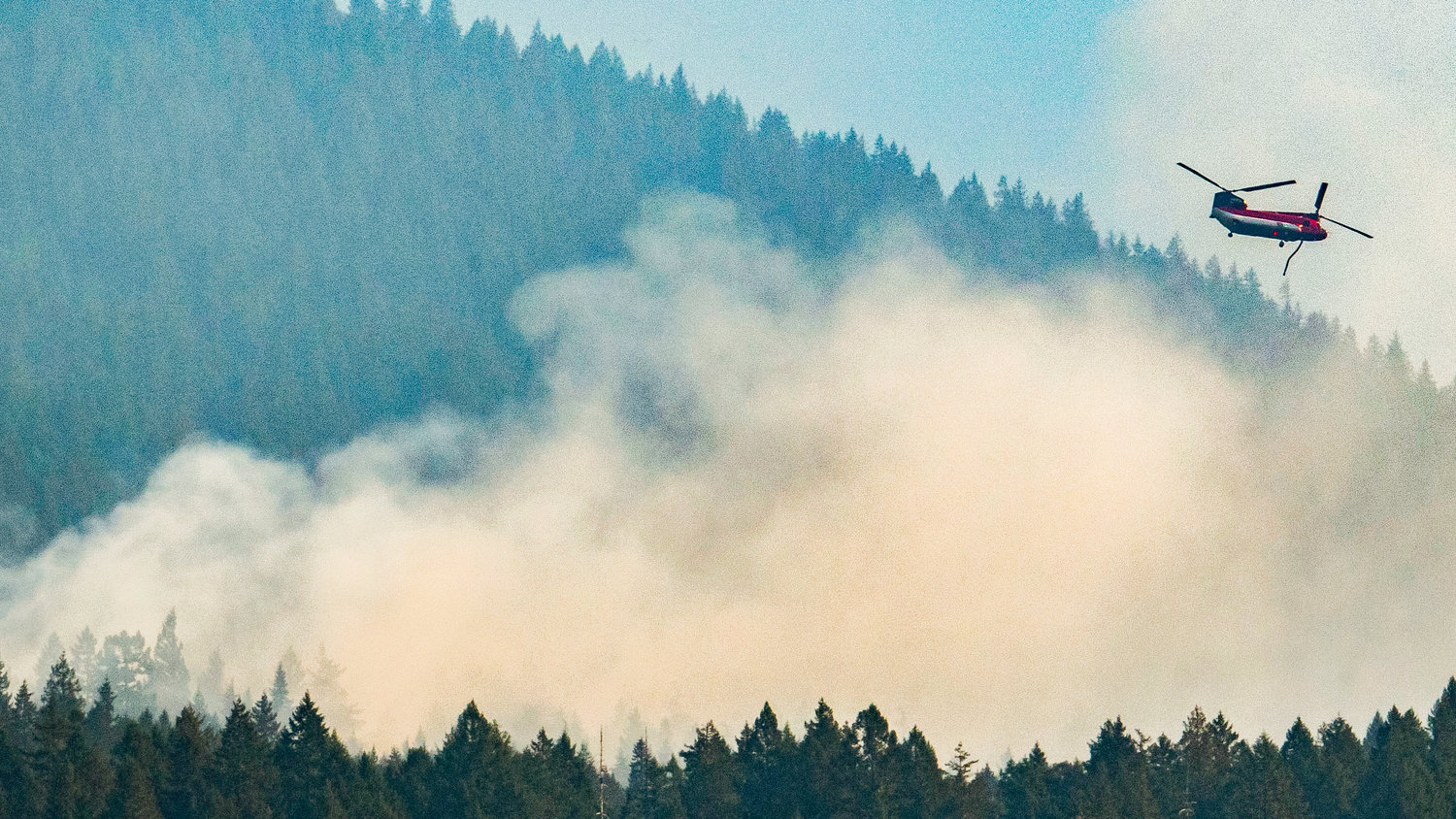In this Chronicle file photo from October 2022, a helicopter steers away after dropping water over the Goat Rocks Fire near Packwood; heavy grain on this photo also illustrates the thickness of the smoke in the air at the time.
